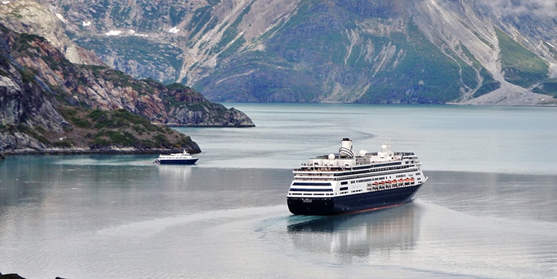A small ship seen cruising near a big cruise ship in a calm Alaska cove.