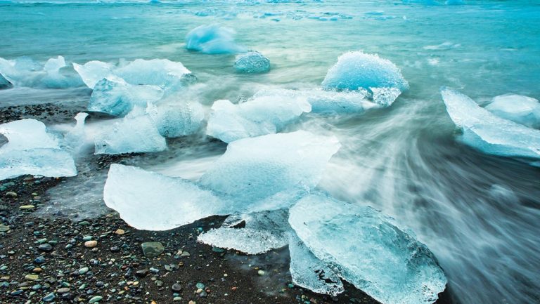 Sheets of crystal teal ice wash ashore to a black sand beach in Iceland seen aboard Wild Iceland Escape Arctic cruise.