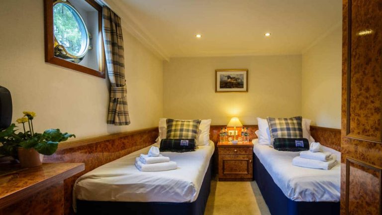 2 twin beds with bedside table between, porthole, & walnut-wood large closet & desk aboard Spirit of Scotland barge.