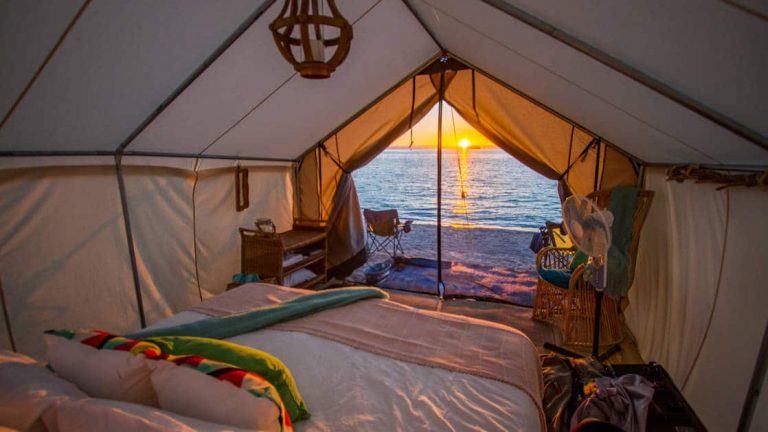 Luxury glamping tent at Camp Cecil on Isla Espritu Santo in Baja, looking out past double bed to sunset over the beach.