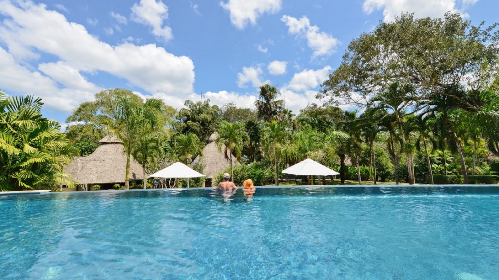 A man and women at the edge of the infinity pool overlooking the jungle and thatched rooves of rooms at the Lodge at Chaa Creek.