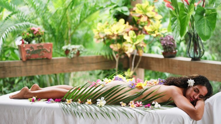Woman peacefully relaxing on a massage table receiving a spa treatment in a private outdoor area surrounded by jungle foliage and flowers in Belize.
