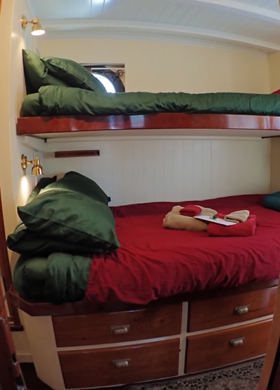 Cabin #1 aboard Catalyst small ship. A bunk bed against a white wall, porthole window and green and red bedding and pillows.