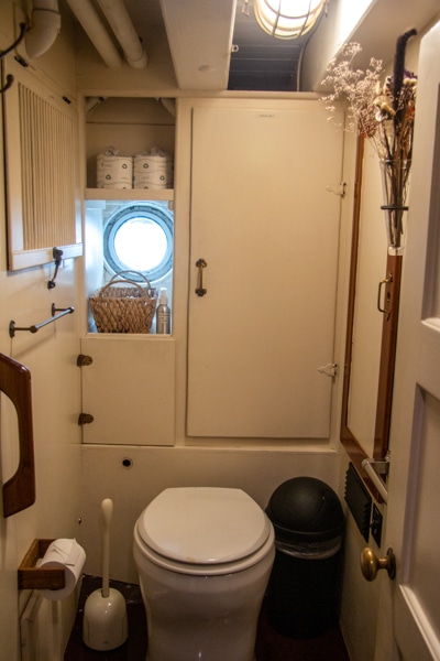 The mainly all white private bathroom inside a cabin aboard Alaska small ship Catalyst with a small porthole toilet and cabinets
