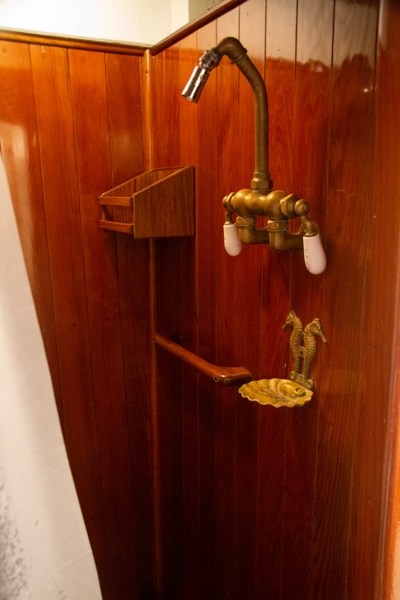 The private shower inside a cabin aboard Alaska small ship Catalyst. A brown wood shower with bronze shower head and soap dish.