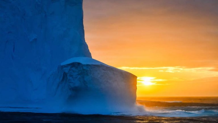 Orange sunset behind tall dark blue glacier seen during Le Commandant Charcot Ross Sea Expedition.