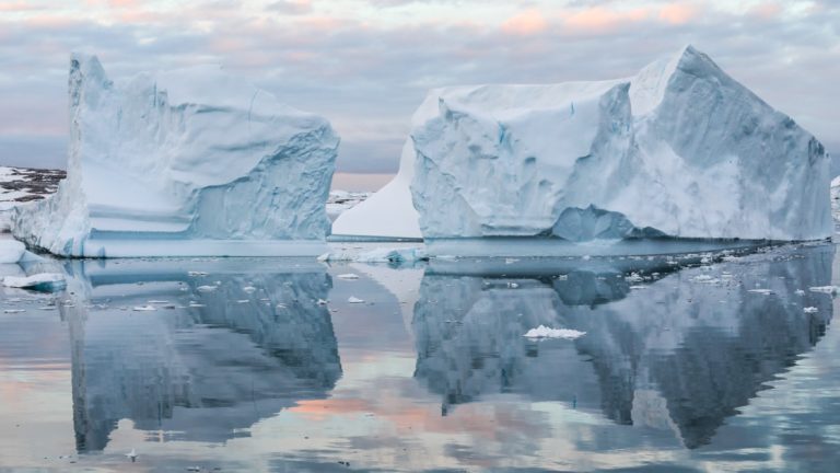 Large icebergs reflect in glassy Antarctic waters at dusk during the Le Commandant Charcot Ross Sea Expedition.