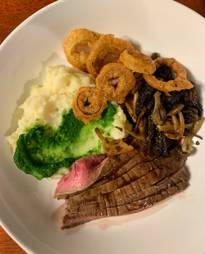 A dinner plate served aboard Alaska small ship catalyst, mashed potatoes, fried onions and steak on a white plate. 