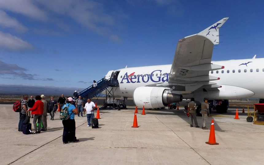 Draußen auf der Landebahn des Flughafens stehen Galapagos-Reisende mit ihrem Gepäck, die darauf warten, in ein weißes Flugzeug mit der Aufschrift Aero Galapagos einzusteigen.