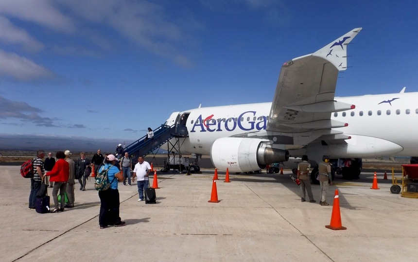 lentoaseman kiitotien ulkopuolella Galapagos-matkustajat odottavat matkatavaroineen pääsyä Aero Galapagos-merkkiseen valkoiseen lentokoneeseen. 