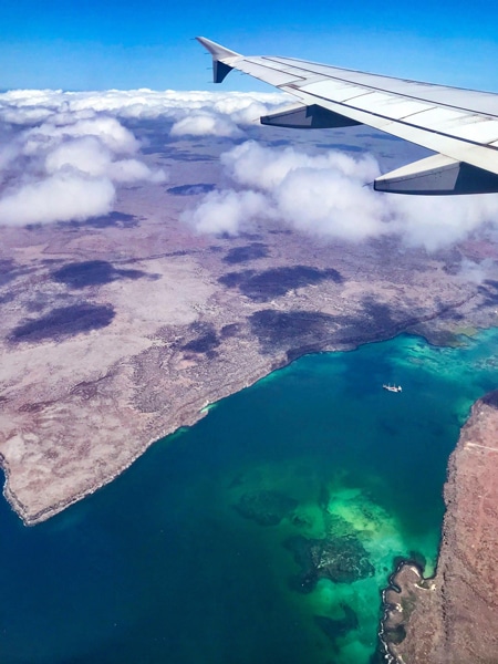  Foto aus dem Galapagos-Flugzeugfenster, Blick über den Flugzeugflügel nach unten und das kristallklare blaue Meerwasser, das die Inseln unten umgibt. 