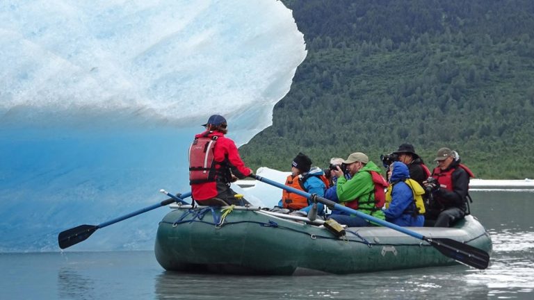 Group of Southcentral Alaska travelers photograph a large iceberg as their tour leader paddles them beside it during the Alaska Explorer trip.