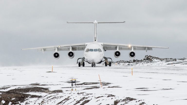 A white snowy landscape on a overcast day, a white charter plane sits on an empty runway ready for Antarctica Air cruises.