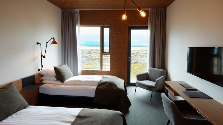 Guest room at Fosshotel Myvatn, with white & wood walls, twin beds with white & green linens, flactscreen TV, wooden desk & lake views.