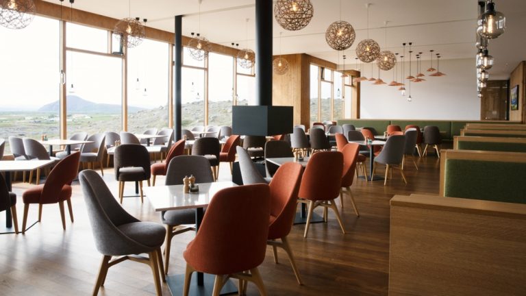 Restaurant at Fosshotel Myvatn, with hanging globe lights, Scandinavian furnirture & wall-to-ceiling windows overlooking the lake.