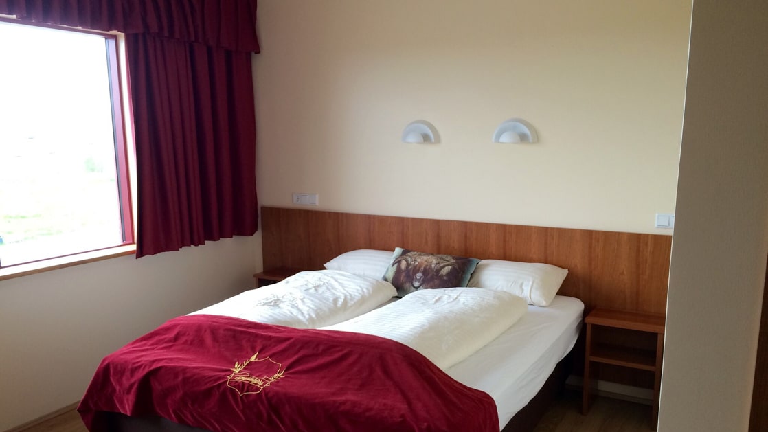 Hotel Smyrlabjorg guest room with double bed, large, bright window & white & red velvet accents.