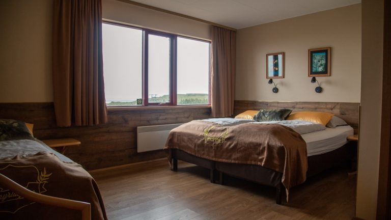 Hotel room with double bed, twin bed, large window, wooden floors & beige & gold accents at Hotel Smyrlabjorg in Iceland.