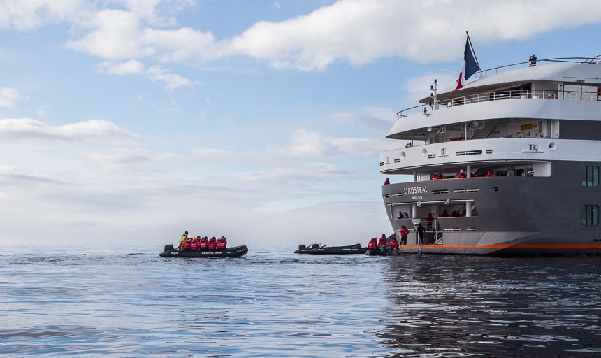 Guests finishing a zodiac excursion disembark the black inflatable rafts onto the stern of a four level luxury ship from Ponant cruise lines.
