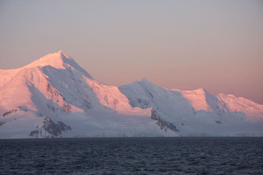 rosa solnedgång nyanser på snötäckta toppar bredvid öppet hav. Ett svar För ska jag åka till Antarktis?