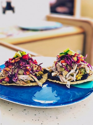 Lunch option from a Belize sailboat charter. A blue plate with two tacos filled with bright colored vegetables and shredded chicken.