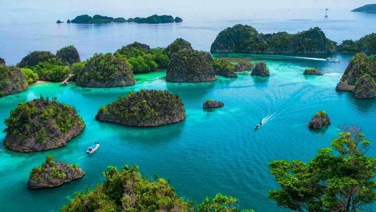 Aerial view of Raja Ampat's tiny islands in emerald waters with small ships cruising past, seen on a cruise to Bali from Australia.