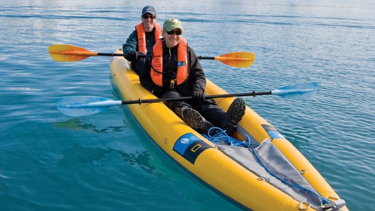 Tandem kayakers in a yellow inflatable sit-on-top boat hold paddles still on the National Geographic Northwest Passage voyage.