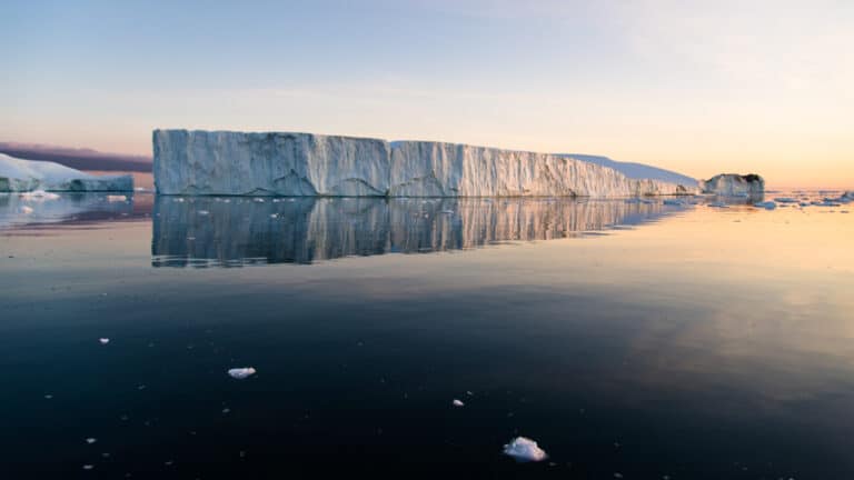 Large iceberg floats in glassy water at dusk, seen on Le Commandant Charcot Svalbard Voyages.