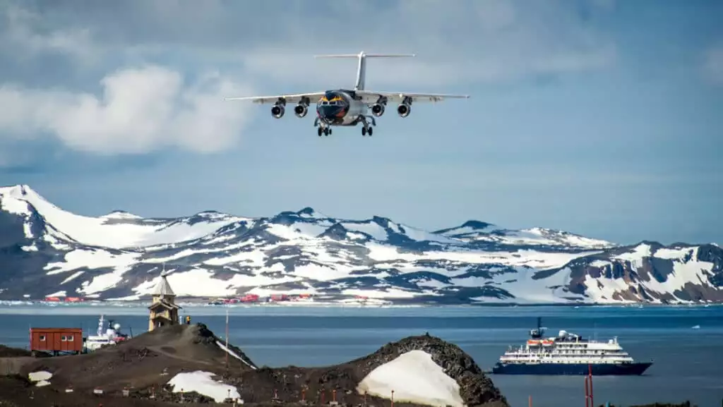 A sunny blue sky day in Antarctica as a flight lands at Frei Station with a ship seen anchored