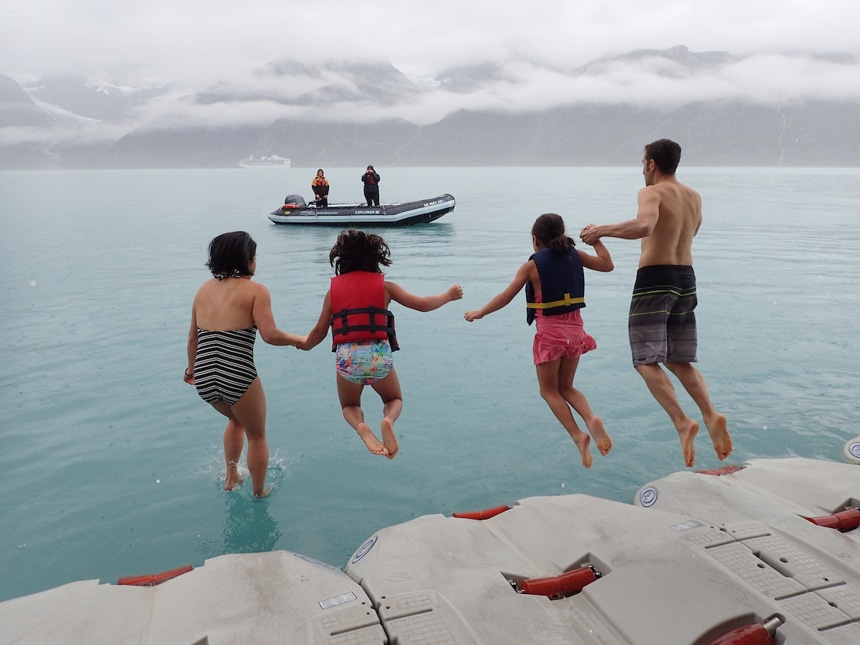 A family of 4 hold hands and jump from the boat platform into the icy cold water of alaska, braving the polar plunge.