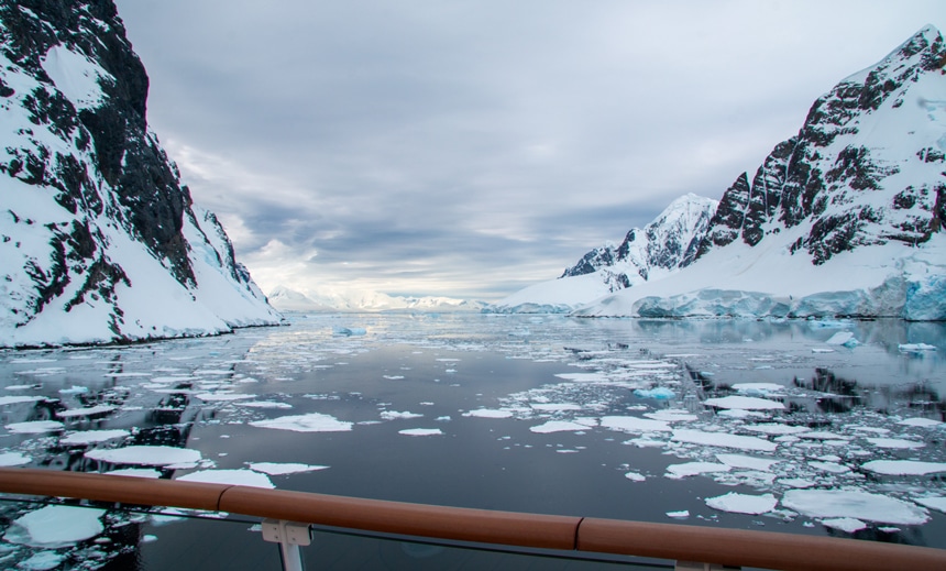An icy mountainous Antarctica landscape taken from a ship as it passes through a water channel filled with floating ice chunks.