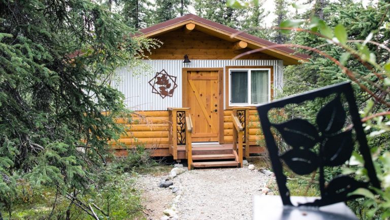Exterior of a small, modern log cabin at Denali lodge Tonglen Lake, with window, front steps & wrought iron artwork