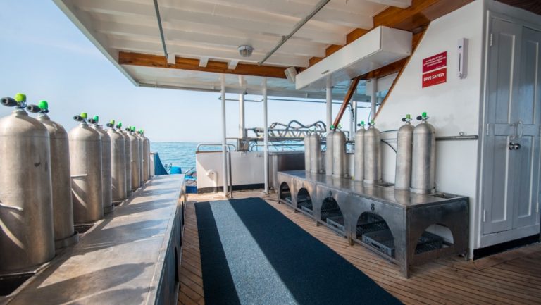Dive deck of mv Galapagos Sky with silver oxygen tanks sitting atop metal benches with cubbies below in an open-air format.
