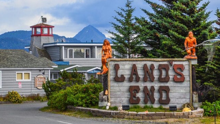 Entrance sign to Land's End Resort in Homer, Alaska, with nautical themed architecture & figurines set amongst mountains.