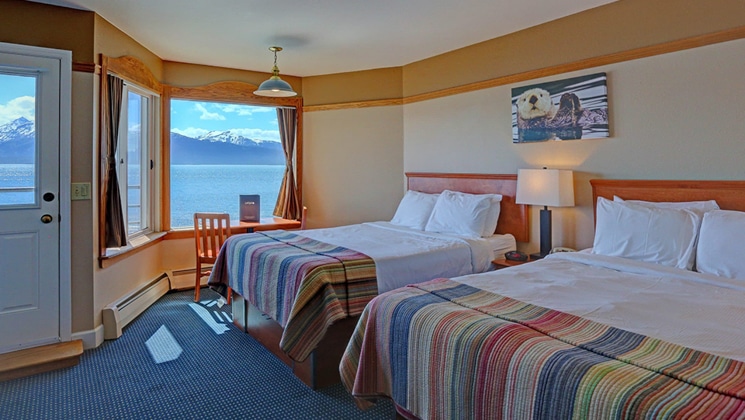 Land's End Resort guest room with 2 double beds, sea views, beige accents, oceanfront door, bedside table & wooden furniture.