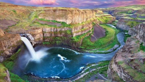 Large waterfall feeds flowing river in green & tan canyon, seen on Pacific Northwest tours.