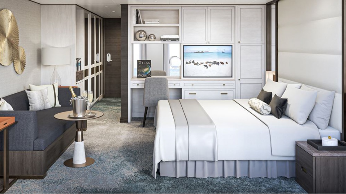Rendering of suite on Nat Geo Islander II Galapagos ship with modern beige decor, double bed, dark blue sofa, desk & champagne.