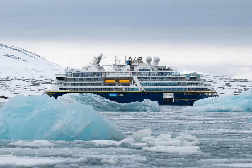 A Svalbard expedition vessel navigates an icy ocean of teal floating icebergs near the shoreline of the Svalbard archipelago