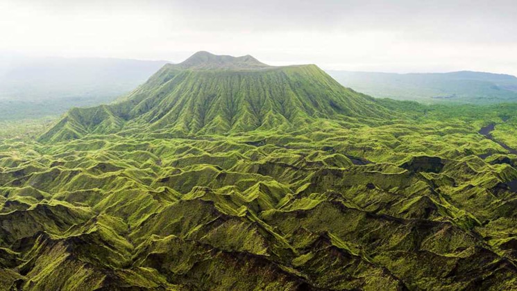 Aerial view of a verdant green volcano with smaller green mountaintops in the foreground, seen on Under The Southern Cross cruise.