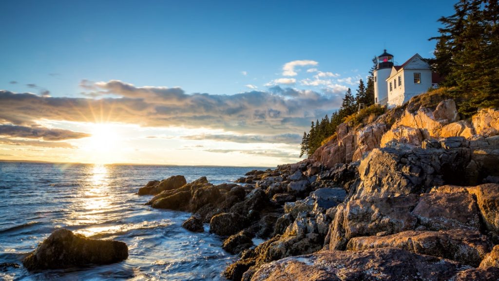 White Bass Harbor lighthouse sits atop jagged rock beside evergreen forest on the Wild Maine Escape Acadia National Park cruise.