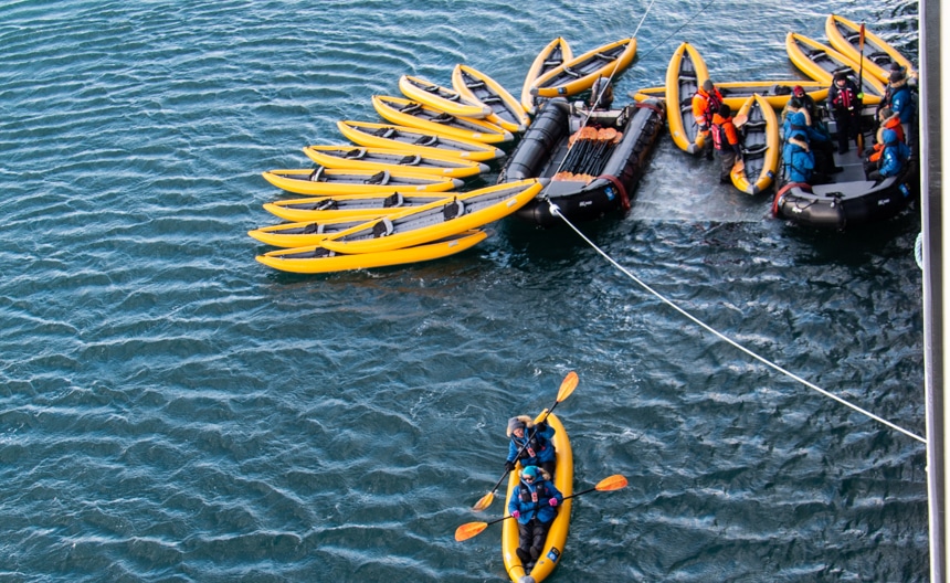 Aboard Nat Geo Resolution. guest load into yellow Kayaks one at a time, on a shallow platform suspended between two black zodiacs.