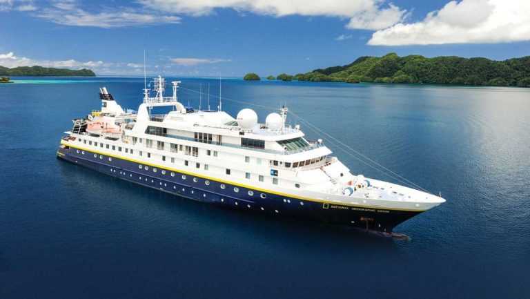 Aerial view of National Geographic Orion ship with dark blue hull & white upper decks during a South Pacific Cruise.