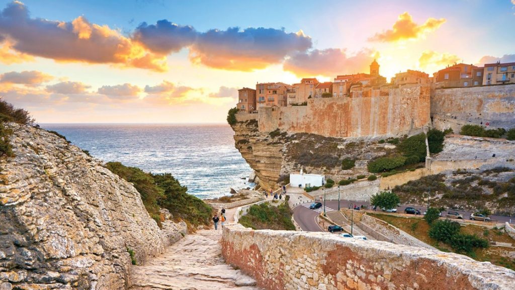 Stone steps lead down to the sea with cliffside stone buildings above at sunset, seen sailing the Western Mediterranean.