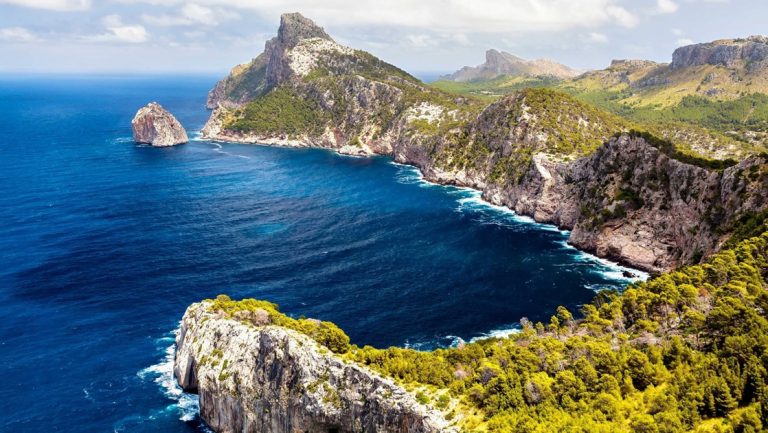Aerial view of a deep blue sea lining bright green cliffs & jagged peaks seen sailing the Western Mediterranean aboard Sea Cloud.