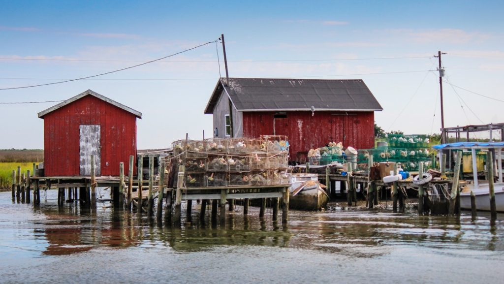 Weathered red fishing huts on docks with crab pots & netting sitting over calm water, seen on Chesapeake Bay overnight cruises.