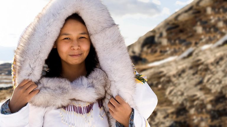 A young Inuit girl, arctic indigenous people of Greenland, dressed in traditional clothing of a thick hood made of white animal fur